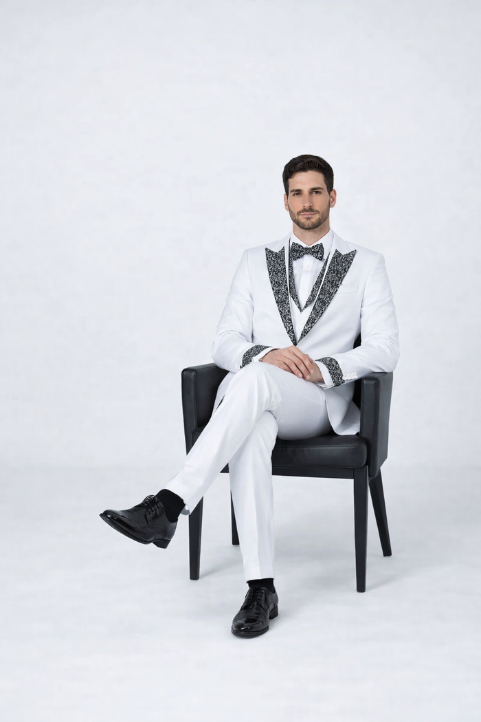 Men's white wedding tuxedo: fitted jacket with black lapel & cuff detailing, slim pants, and matching bow tie. Smooth fabric, formal look. Completed with black dress shoes for a sophisticated appearance.
