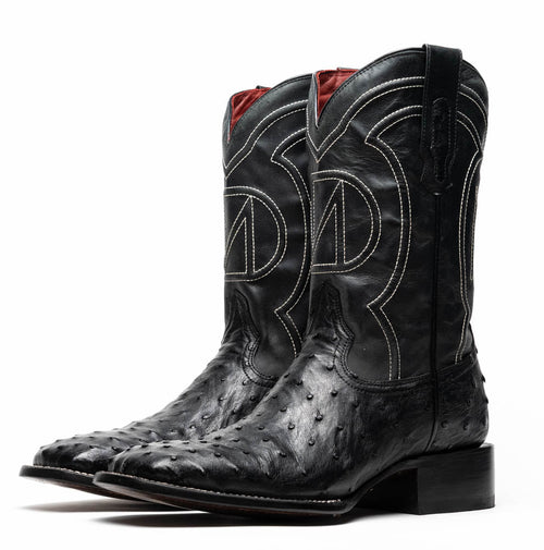 Black ostrich quill cowboy boots by Marco Di Milano. Square toe, raised heel, and white stitching on the shaft with a curved motif. Red fabric lining.
