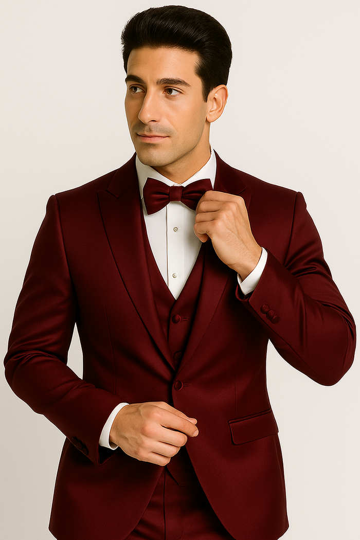 Burgundy Majesty tuxedo: fitted blazer (notched lapel, pockets), matching vest, white dress shirt (classic collar), and burgundy bow tie. Cohesive, formal ensemble.
