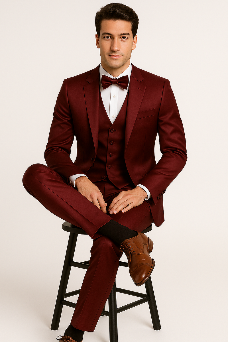Burgundy Majesty tuxedo: fitted jacket (notched lapel, single-button), vest (5-button, pointed), tailored slim-fit trousers, and bow tie. Rich burgundy, smooth, shiny fabric.