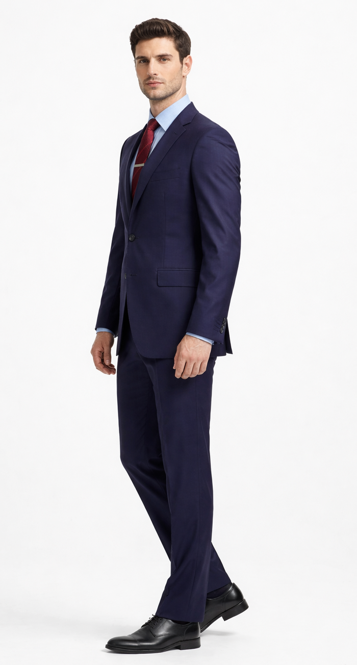 Carlo Lusso navy two-button suit in poly blend. Tailored fit with structured silhouette. Features notch lapels, side pockets, and straight-cut pants. Worn with a blue shirt, navy tie, and black dress shoes.
