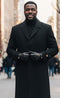 Men's black, single-breasted, full-length topcoat. Tailored straight cut with collar. Dark matte fabric. Button closure and slightly flared sleeves with cuff buttons.
