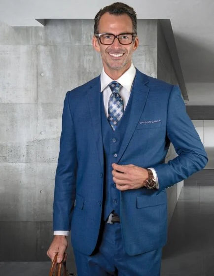 Statement men's three-piece fashion suit features a fitted shape with a subtle texture, made from 100% wool. The suit is primarily a medium blue color, complemented by a white dress shirt and a checkered tie in various shades of blue and gray.