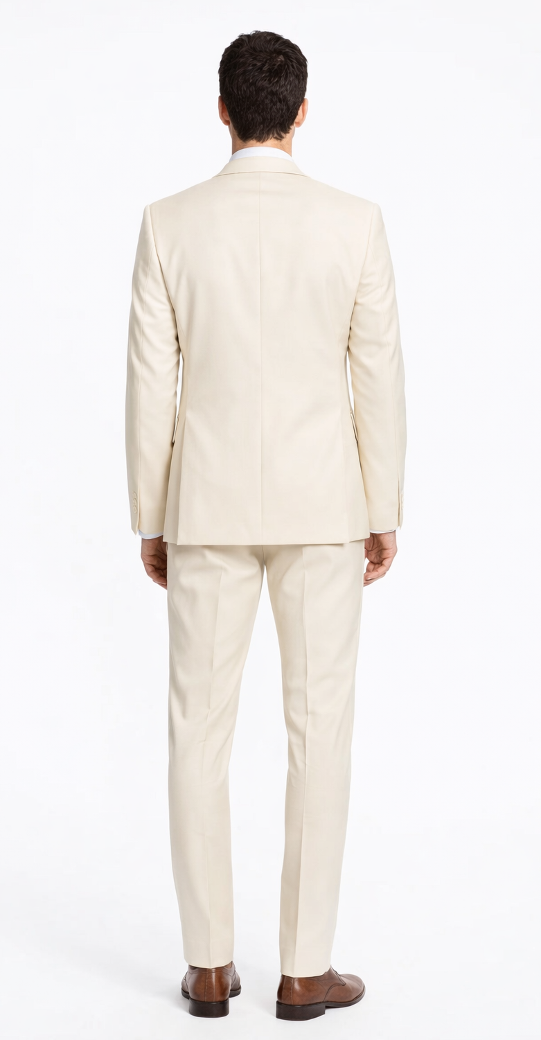 Cream-colored tailored suit with a smooth finish. Jacket: single vent, side pockets. Trousers: straight-legged. Paired with dark brown shoes.
