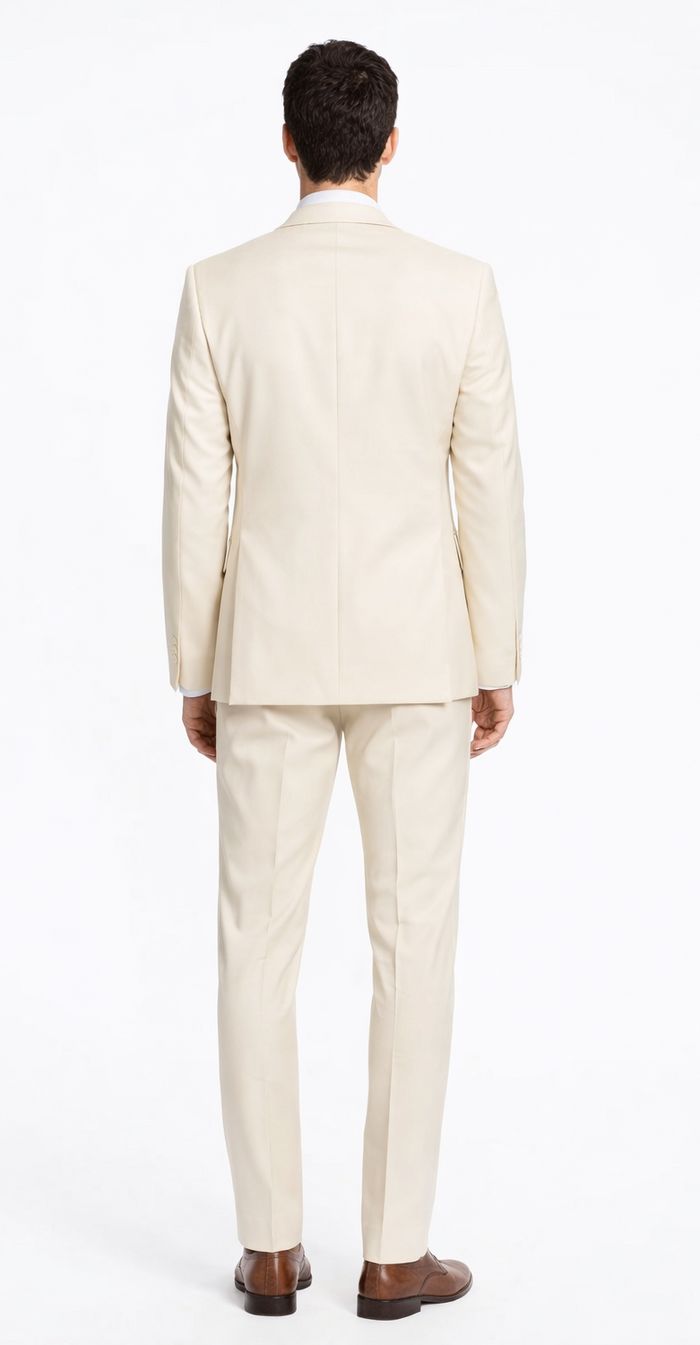 Cream-colored tailored suit with a smooth finish. Jacket: single vent, side pockets. Trousers: straight-legged. Paired with dark brown shoes.
