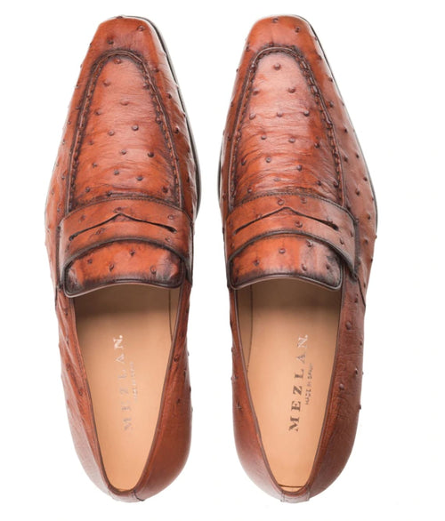 Mezlan's Lisbon Brandy Slip-On: Smooth, elongated shape with textured brown ostrich leather. Rounded toe, stitched moc toe, and flat heel. Features a distinctive pattern and a beige interior lining.
