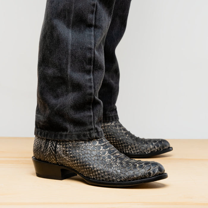 Marco Di Milano Kansas Stone White cowboy boots with a rounded toe, low heel, and textured, dark-colored outer material (possibly snakeskin). Fitted ankle. Flat sole, sleek construction.
