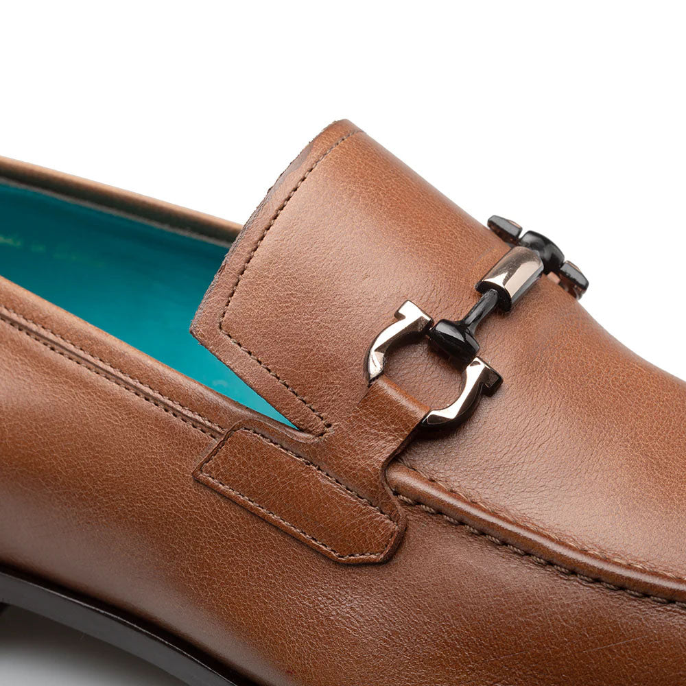 Cognac Mezlan Rios Flex loafer: smooth, glossy leather, black/silver ornament, rounded toe. Turquoise lining contrasts cognac exterior. Subtle stitched detail.
