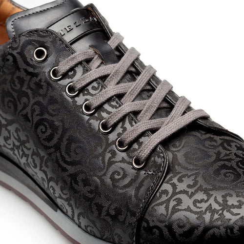 Black Mezlan Portico sneaker with laser-printed pattern. Features a textured upper, round toe, and grey laces. Contrasting rubber sole with embossed logo on the tongue. Predominantly black with subtle shade variations.
