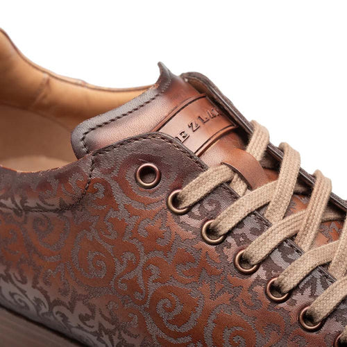 Cognac rust Mezlan Portico sneaker. Laser-printed textured leather upper with swirl pattern. Rounded toe, tan tongue with logo. Brown eyelets, beige laces, rubber sole.
