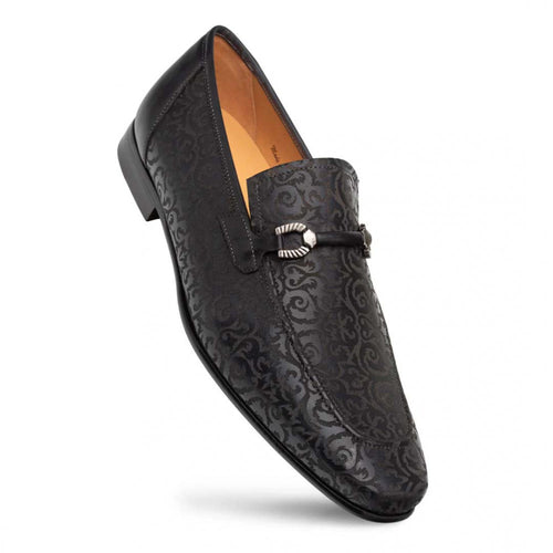 Mezlan Alcaraz black slip-ons: elongated shape, slight heel. Textured exterior with laser-printed pattern. Decorative strap with metallic buckle. Light-colored interior lining.
