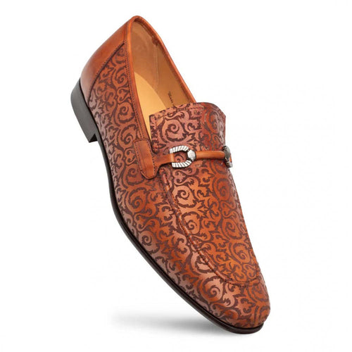 Mezlan Alcaraz cognac slip-ons: Pointed toe, laser-printed leather upper with swirling design, metal buckle detail. Low heel, polished finish. Warm cognac color palette.
