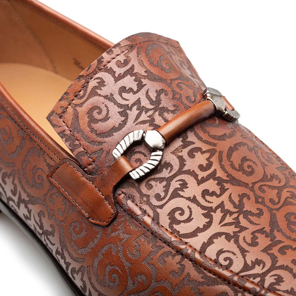 Cognac Mezlan Alcaraz slip-ons with laser-printed swirling design, metallic strap, and a cohesive leather color scheme. Smooth, rounded shape.

