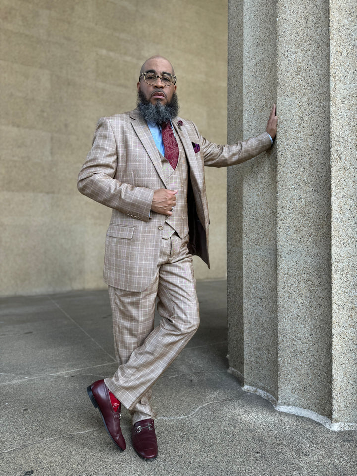 Camel plaid windowpane suit with peak lapels, two-button closure, and a fitted silhouette. Includes matching trousers and a tailored vest worn beneath the jacket.
