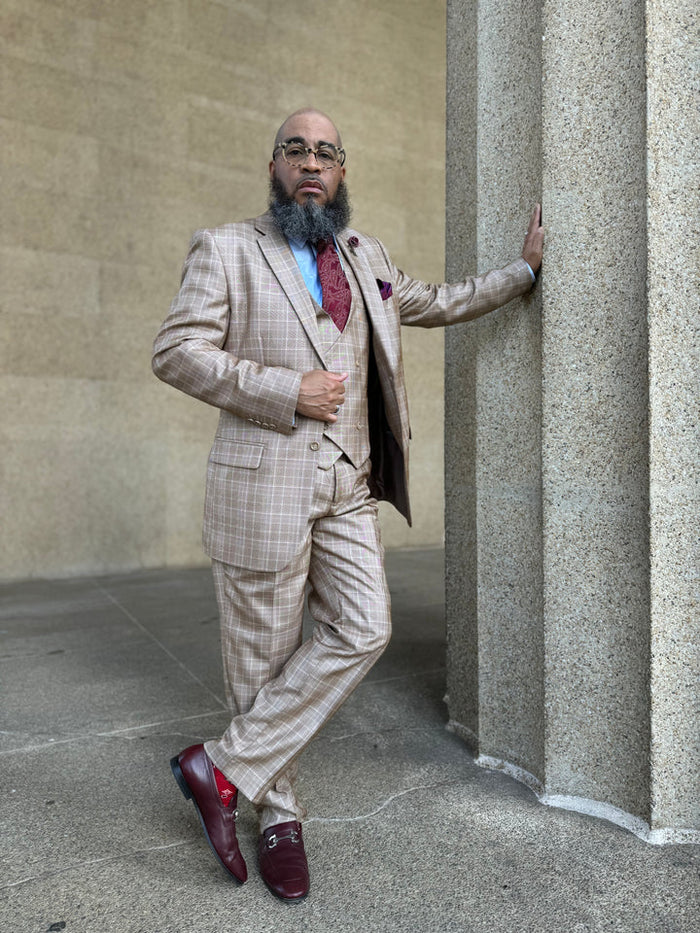 Camel plaid windowpane suit with peak lapels, two-button closure, and a fitted silhouette. Includes matching trousers and a tailored vest worn beneath the jacket.
