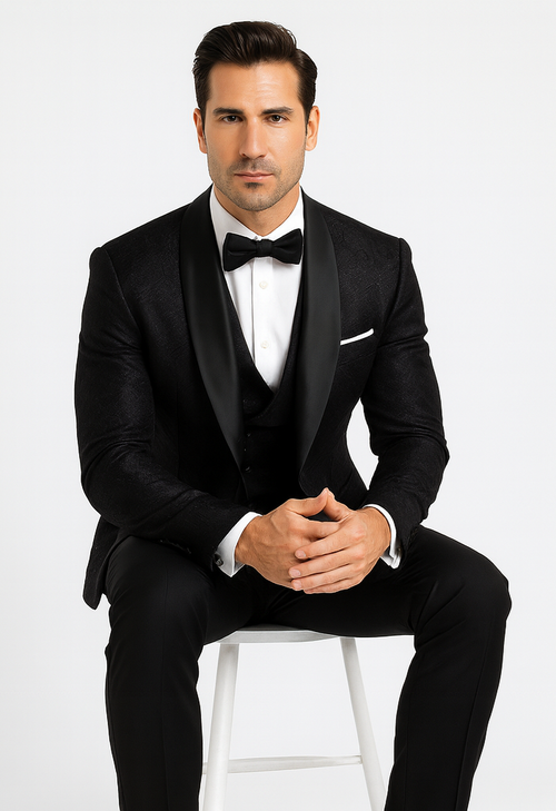 Black floral lace tuxedo for men, tailored fit. Includes vest, bow tie, and white shirt. Sleek lapels, textured floral pattern, and black pants create an elegant, formal look.
