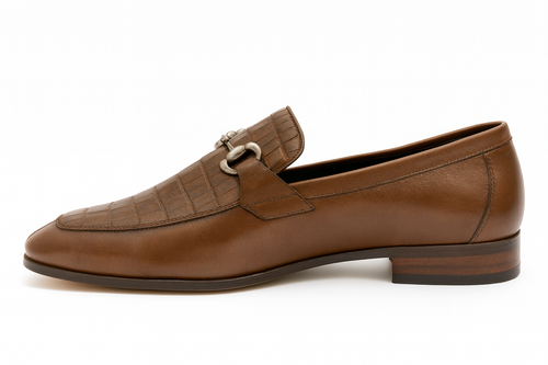 Men's brown leather slip-ons with stitched vamp detail. Rounded toe, low stacked heel, and metal buckle accent. Rich brown color with tone variations, sleek profile.
