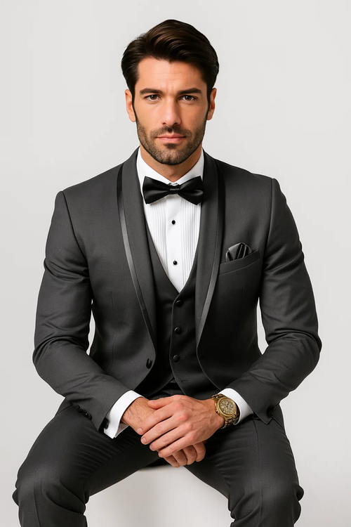 Charcoal satin tuxedo suit with shawl lapel, single-breasted. Includes vest with three buttons, tailored trousers, white shirt, and black bow tie. Features pocket square. Smooth, shiny fabric.
