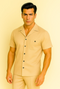 Men's sand-colored leisure suit: short-sleeve shirt with pointed collar, breast pocket, black buttons, and matching fitted pants. Lightweight, smooth fabric.
