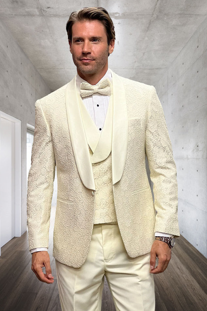 Ivory designer tuxedo with fitted shape & floral lace. Satin shawl collar, matching vest, & ivory trousers complete the elegant men's ensemble.
