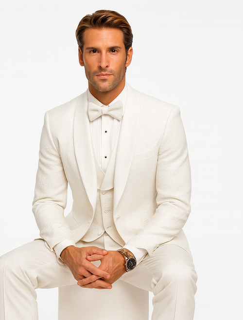 Men's white designer tuxedo with textured floral lace, structured jacket, notch lapels, and vested tunic. Includes tailored trousers, bow tie, and pleated dress shirt for a fitted look.
