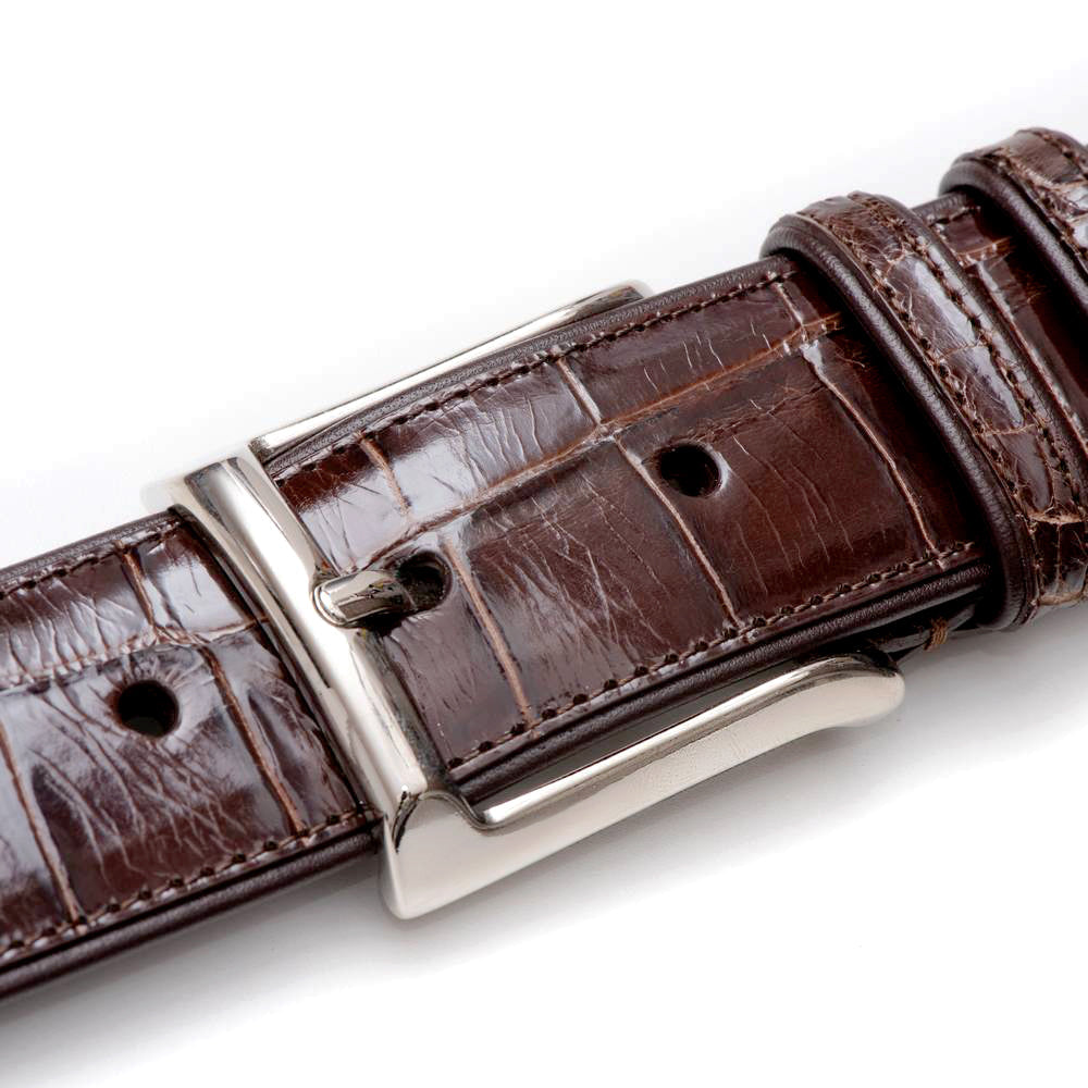 Dark brown Mezlan alligator belt. Textured, glossy finish. Silver rectangular buckle. Adjustable with evenly spaced holes. Distinctive alligator scale pattern.
