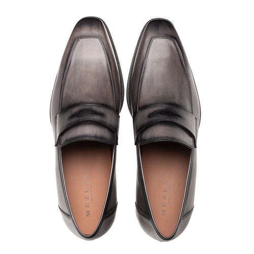 Dark grey Mezlan penny loafers with a sleek, rounded shape. Smooth leather upper with raised penny strap. Features a contrasting tan interior and rubber sole.
