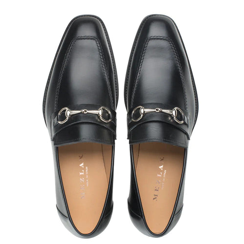 Black Mezlan leather loafers with a sleek, elongated design and squared toe. Features a silver ornament on the vamp and visible stitching. Low-profile sole with curved heel.
