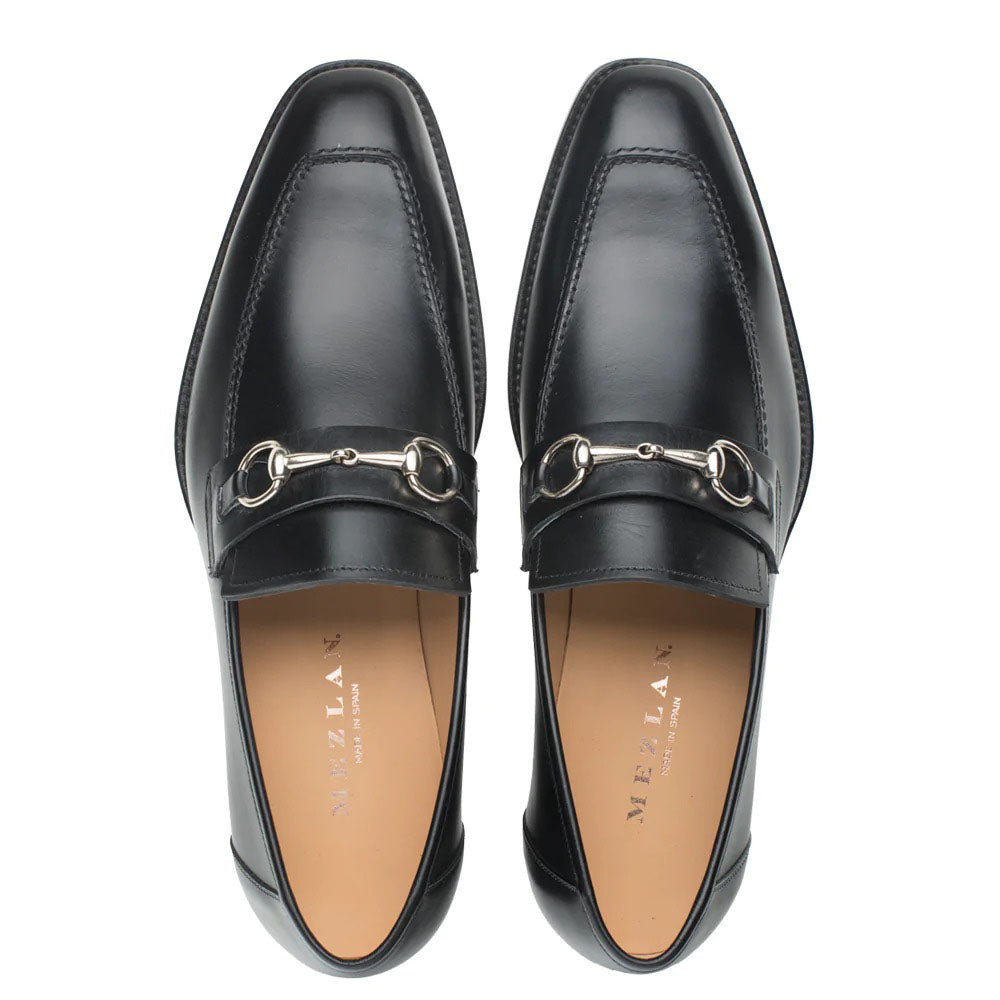 Black Mezlan leather loafers with a sleek, elongated design and squared toe. Features a silver ornament on the vamp and visible stitching. Low-profile sole with curved heel.
