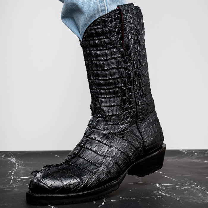 Marco Di Milano Marlboro cowboy boots in black hornback crocodile. Tall shaft, pointed toes, and distinctive scale pattern. Features a robust tractor sole and red edge stitching.
