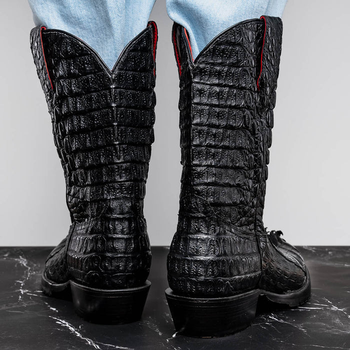 Black hornback crocodile cowboy boots. Textured scales, pointed V-top, red stitching. Tractor sole. Tall, fitted leg. Robust appearance.
