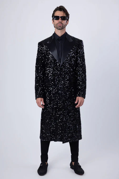Men's black sequin long coat with satin shawl lapel. Straight cut, floor-length. Fully covered in reflective black sequins for a textured look. Long sleeves, contrasting satin lapel, all black.
