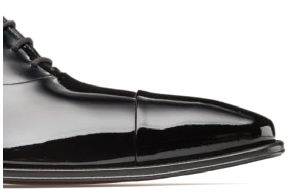 Black patent leather Oxford shoe. Sleek, pointed toe, glossy finish. Uniform black color, subtle curve, thin flat sole. Lacing with evenly spaced eyelets.
