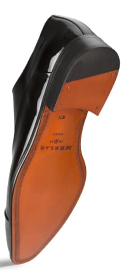 Mezlan's black patent leather Oxford features a shiny upper, rounded toe, and low heel. Its tan leather sole displays curved contours. A sleek and stylish shoe.
