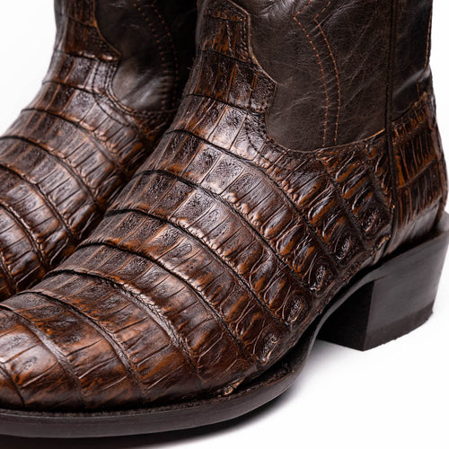 Brown caiman cowboy boots. Round toe, textured scales, dark leather accents, and visible stitching. Low block heel.
