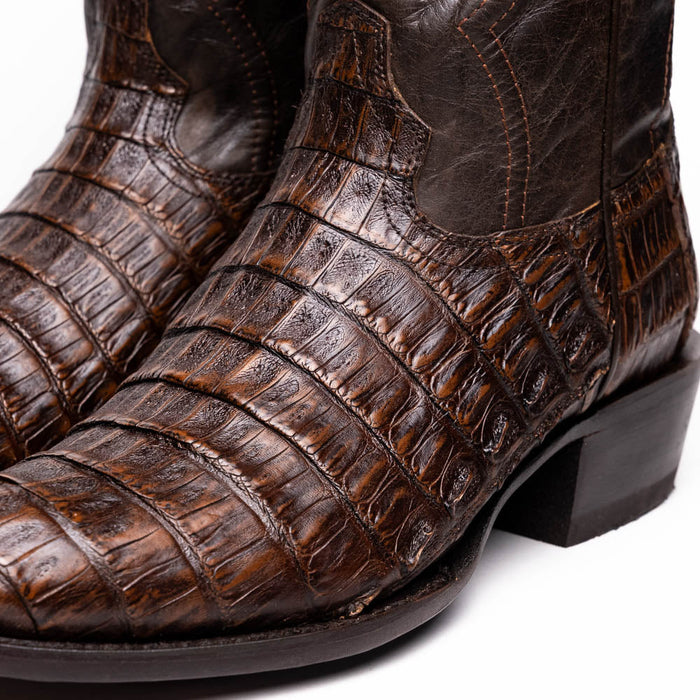 Brown caiman cowboy boots. Round toe, textured scales, dark leather accents, and visible stitching. Low block heel.
