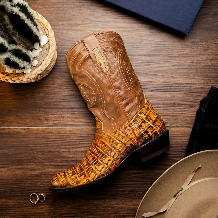 Mustard brown caiman crocodile cowboy boot by Marco Di Milano. Features a round toe, tall shaft, and textured exterior. Upper is smooth leather, lower is patterned caiman skin. Includes visible stitching and a stacked, polished heel.
