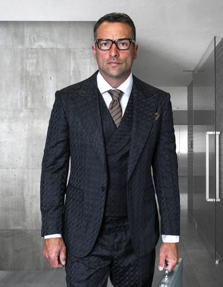 The Statement mens 3 piece fashion suit features a unique checker pattern with a deep navy coloration. The jacket has a tailored fit and is structured with defined lapels. The vest beneath complements the jacket and is also in navy, continuing the checker motif.