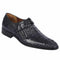 Navy crocodile calfskin slip-on shoes with pointed toe and low profile. Textured surface, dark navy leather. Simple strap with buckle. Black sole, slight heel. Sleek design.
