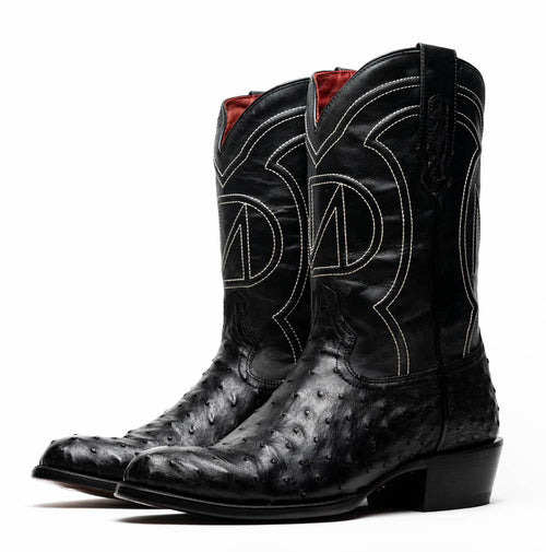 Black ostrich quill cowboy boots by Marco Di Milano. Tall shaft with curved top, textured leather, round toe. Moderate stacked heel. White stitching design, red lining, pull tabs. Ostrich skin texture.
