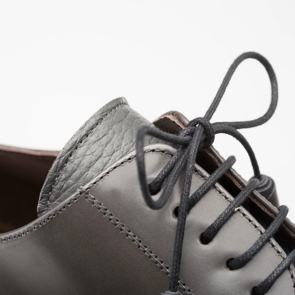 Mezlan Soka cap-toe shoes in gray. Smooth gray calfskin upper with a deerskin collar. Black laces, visible stitching, and classic cap-toe design.
